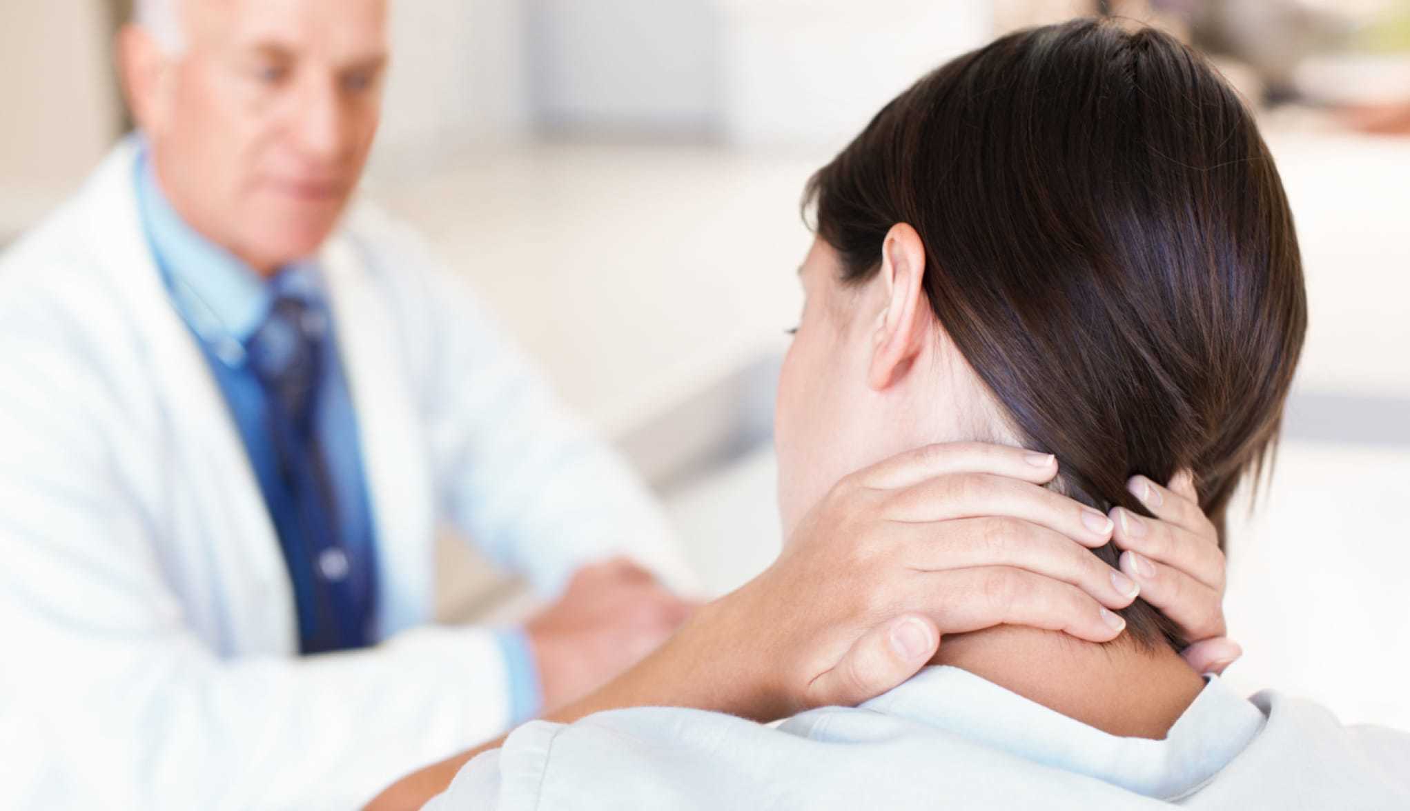 Ratgeber Rheuma: Junge Frau mit Morbus Bechterew reibt sich beim Arztgespräch den Nacken
