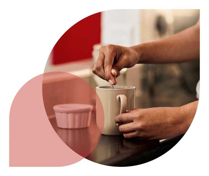 Eine Hand hält einen Löffel in eine Tasse.