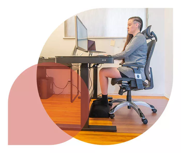 Ratgeber Rheuma: Eine Frau sitzt vor ihrem Bildschirm, ihre Füße ruhen auf einer Fußstütze