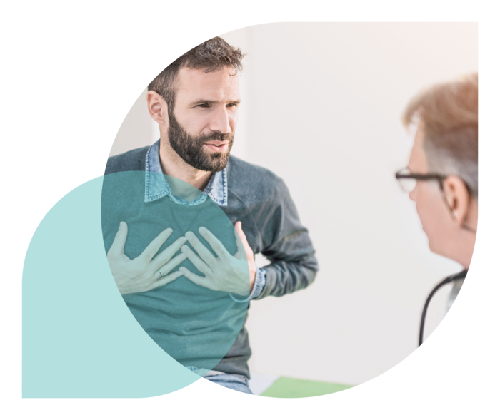 Ein Mann, der sich mit den Händen auf die Brust drückt, im Gespräch mit einem Arzt.