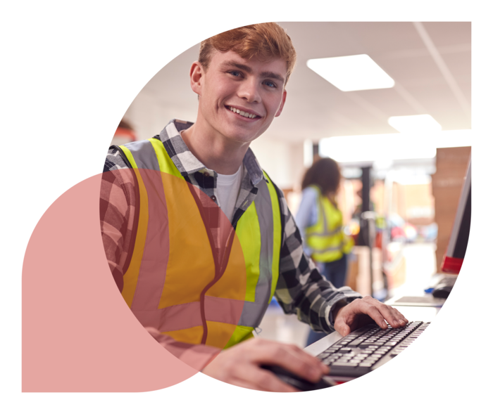 Ein junger Mann mit Arbeitsweste sitzt in einem Lager an einem Computerterminal