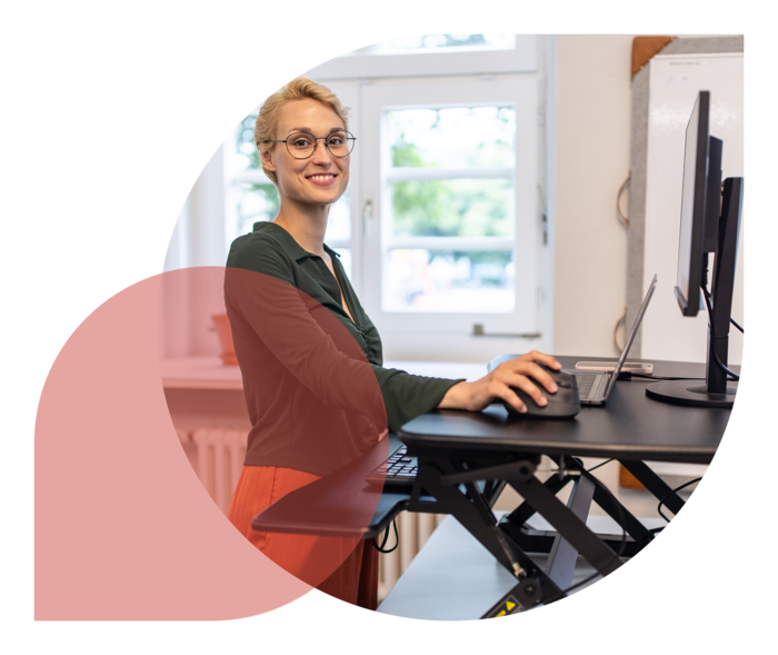 Ein Frau steht in einem Büro an einem höhenverstellbaren Schreibtisch.