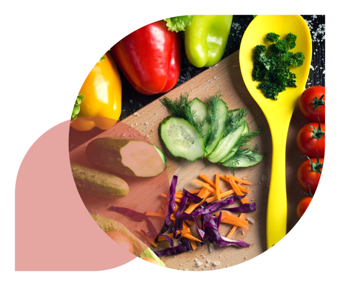 Unterschiedliche Gemüsesorten, eine Schneidebrett und ein gelber Löffel liegen auf einem Tisch.