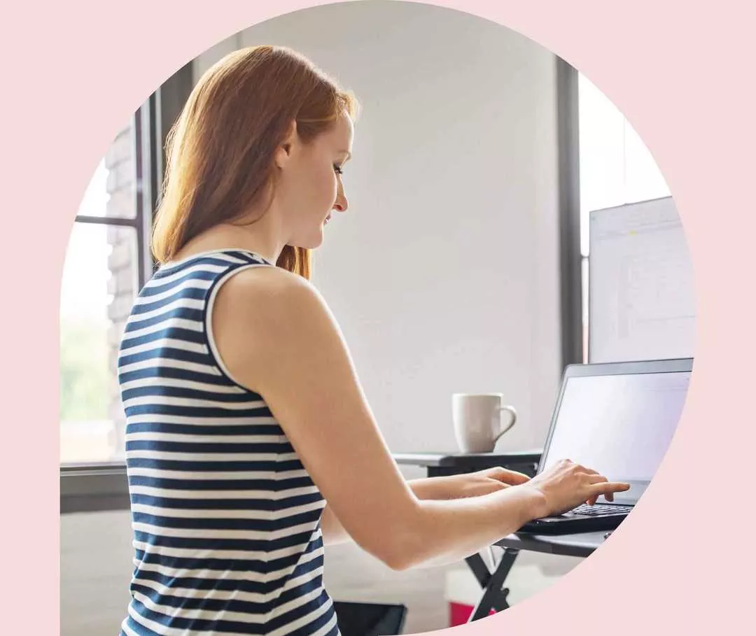 Ratgeber Rheuma: Eine Frau steht an einem höhenverstellbaren Tisch und arbeitet an ihrem Notebook