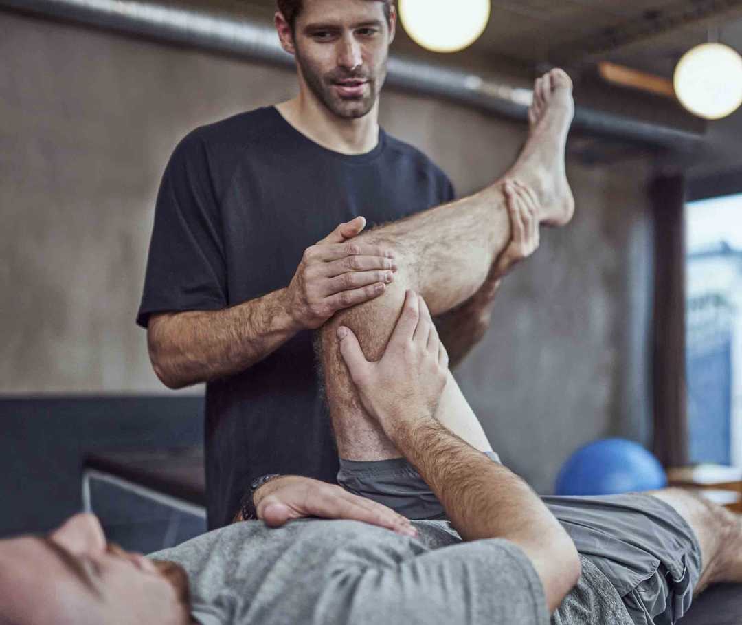 Ratgeber Rheuma: Physiotherapeut macht Beinübungen mit einem an Morbus Bechterew Erkranken