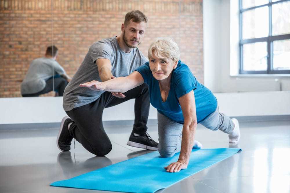Ratgeber Rheuma: Eine ältere Dame macht unter Anleitung eines Physiotherapeuten eine Mobilitätsübung am Boden Ratgeber Rheuma: Eine ältere Dame macht unter Anleitung eines Physiotherapeuten eine Mobilitätsübung am Boden