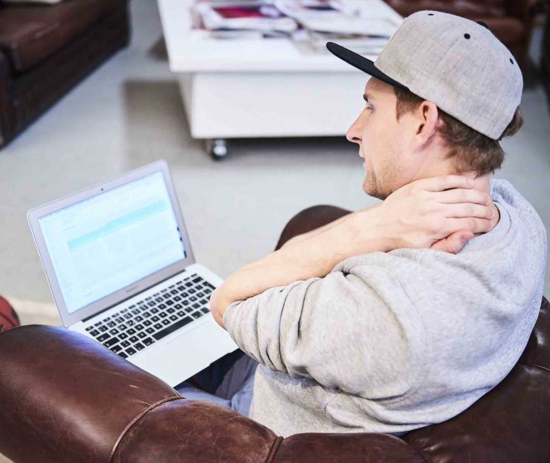 Ratgeber Rheuma: Mann mit Notebook auf dem Schoß reibt sich den verspannten Nacken Ratgeber Rheuma: Mann mit Notebook auf dem Schoß reibt sich den verspannten Nacken
