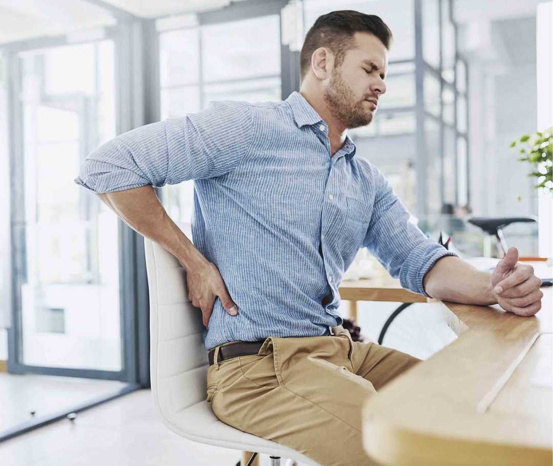 Ratgeber Rheuma: Mann mit Rückenschmerzen sitzt am Schreibtisch