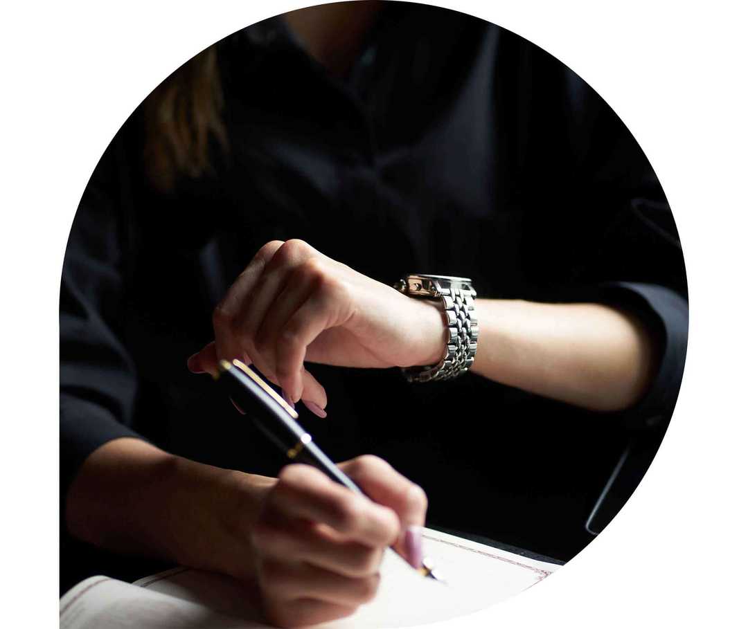 Ratgeber Rheuma: Eine Frau am Schreibtisch schaut auf ihre Armbanduhr Ratgeber Rheuma: Eine Frau am Schreibtisch schaut auf ihre Armbanduhr