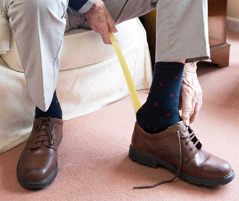 Bechterew: Ein älterer Herr hilft sich mit einem extra langen Schuhanzieher 