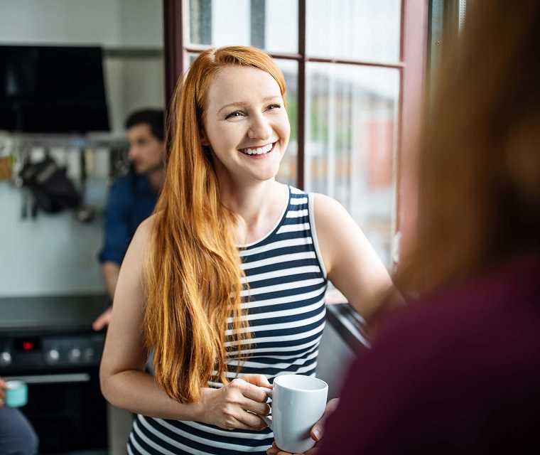 Junge Frau mit roten Haaren lächelt ihre Arbeitskollegin an