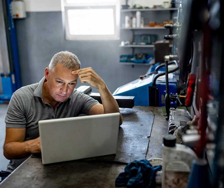 Mann mit grauen Haaren schaut nachdenklich auf seinen Laptop