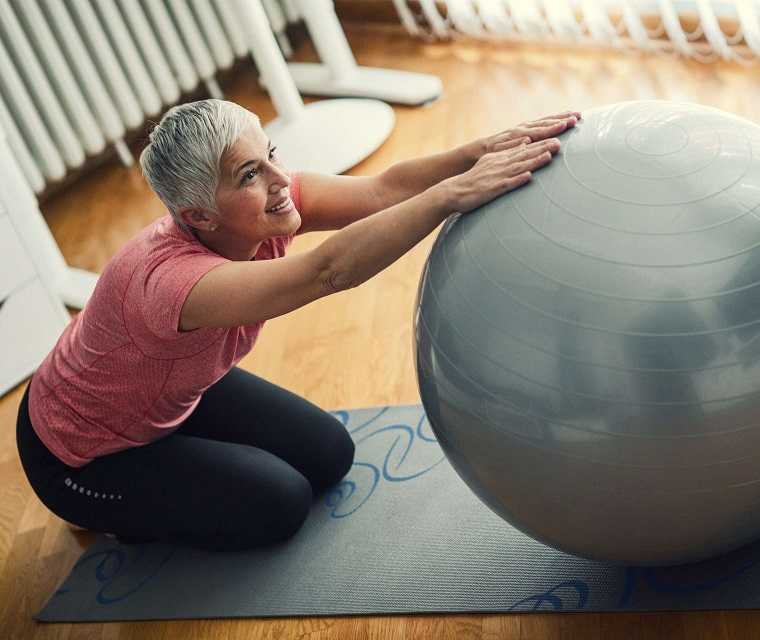 Frau mit grauen Haaren macht Übungen mit einem Gymnastikball