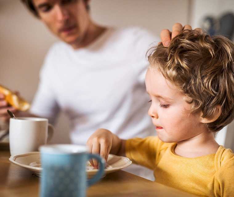 Vater streichelt den Kopf seines Kindes am Frühstückstisch