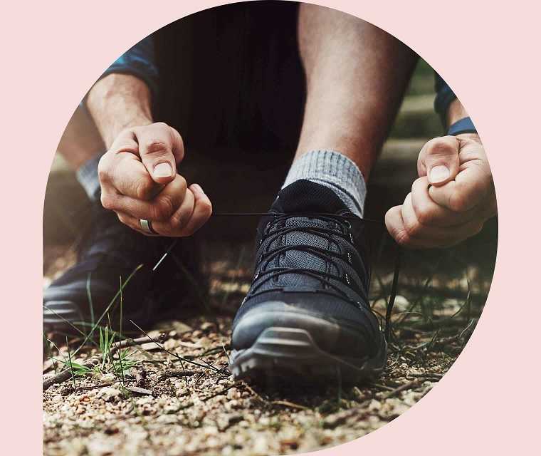 Nahaufnahme zweier Hände, die einen Wanderschuh zuschnüren. 