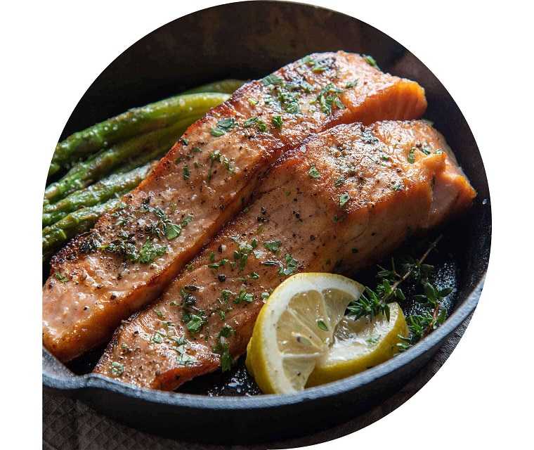 Zwei Lachsfilets in einer Pfanne mit Zitrone und Kräutern.