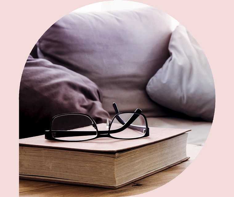 Nahaufnahme von Tasse und Buch mit Brille auf Holztisch vor der Couch im Wohnzimmer Nahaufnahme von Tasse und Buch mit Brille auf Holztisch vor der Couch im Wohnzimmer