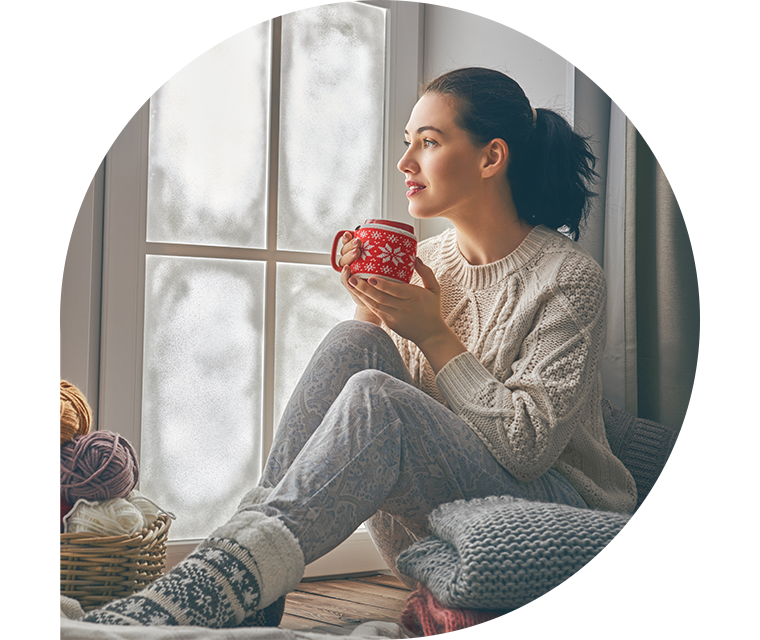 Ratgeber Rheuma: Eine nachdenkliche Frau sitzt mit einer Tasse Tee auf einem Fensterbrettgt die Tatoos auf ihrem angespannten Arm