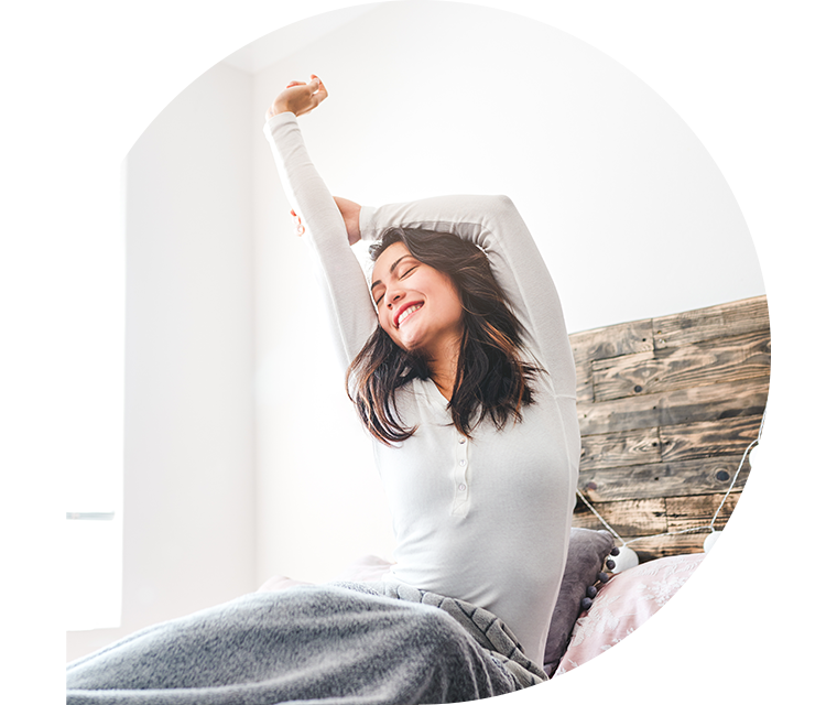 Eine Frau reckt sich in ihrem Bett gut gelaunt nach einem ausgiebigen Schlaf