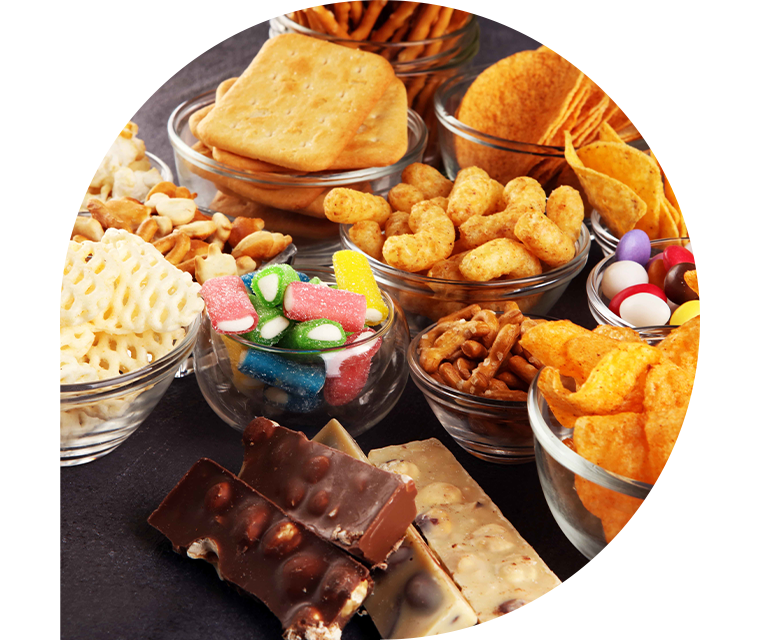 Auf einem Tisch stehen salzige Snacks wie Chips und Cracker sowie Süßigkeiten in Form von Schokolade und Bonbons