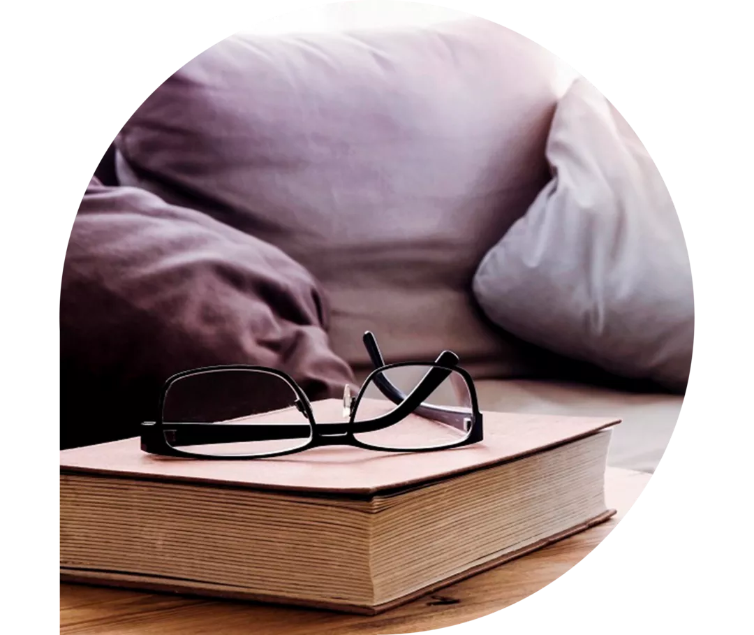 Nahaufnahme von Tasse und Buch mit Brille auf Holztisch vor der Couch im Wohnzimmer 