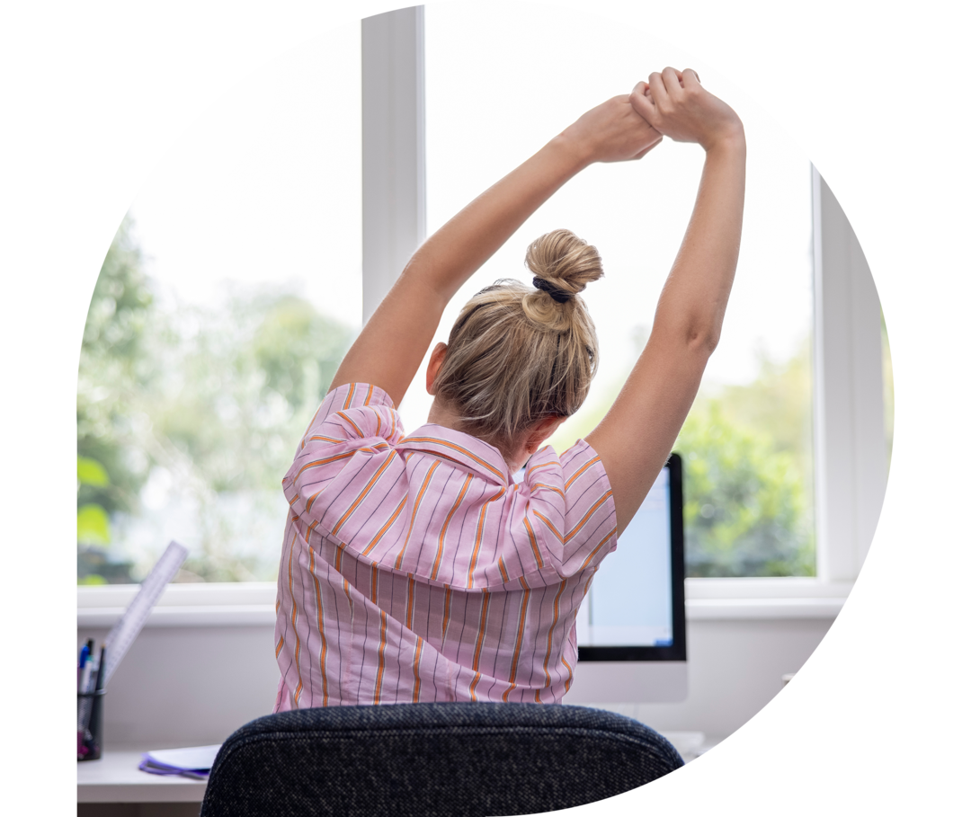 Eine Frau streckt sich an ihrem Schreibtisch
