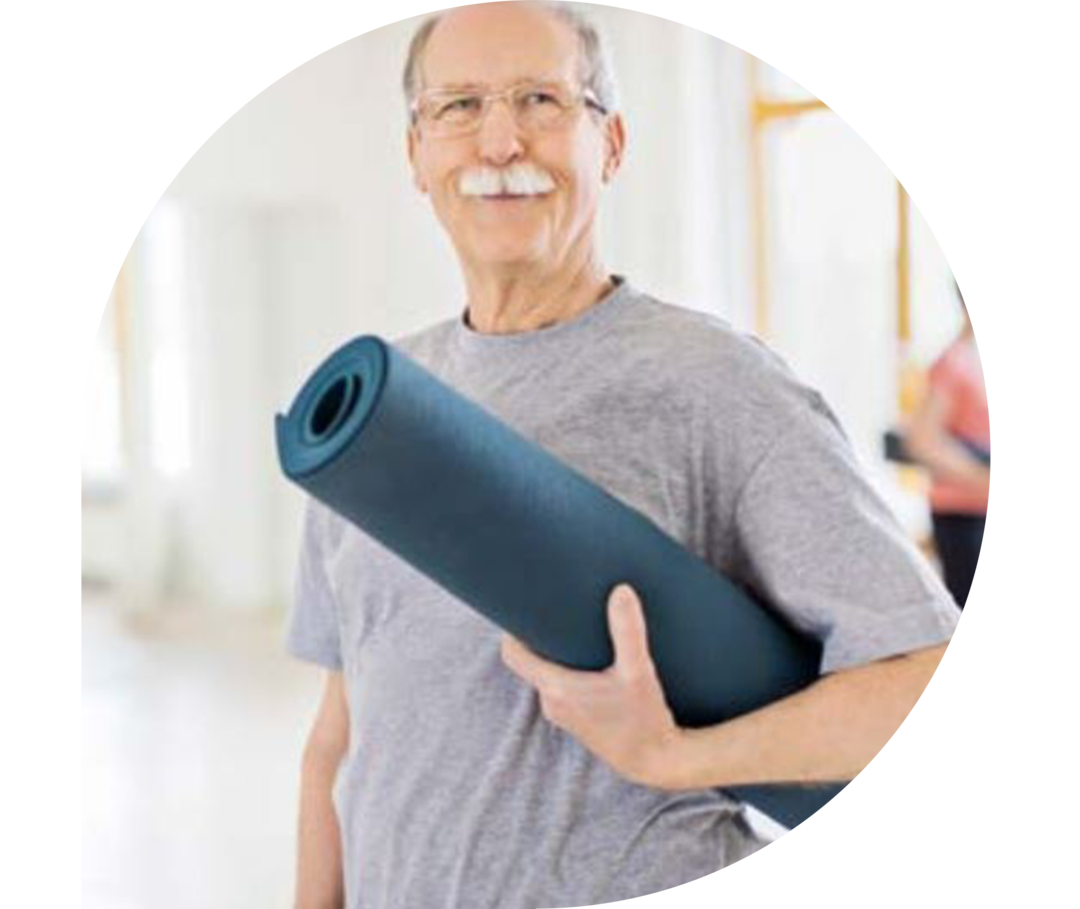 Porträt eines lächelnden älteren Mannes, der in der Yogastunde steht. Er trägt Sportkleidung und eine Yogamatte unterm Arm.