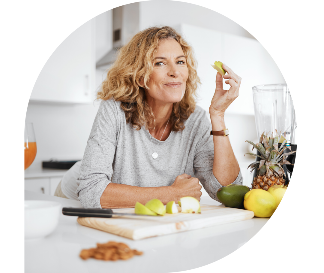 Eine Frau sitzt in einer Küche und isst Obst.