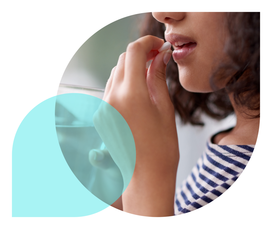 Eine junge Frau nimmt eine Tablette ein und hält ein Glas Wasser in der Hand.