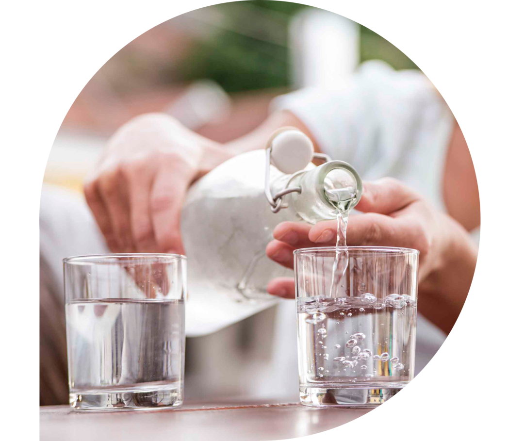 Eine Frau füllt zwei Gläser mit Wasser aus einer Flasche.