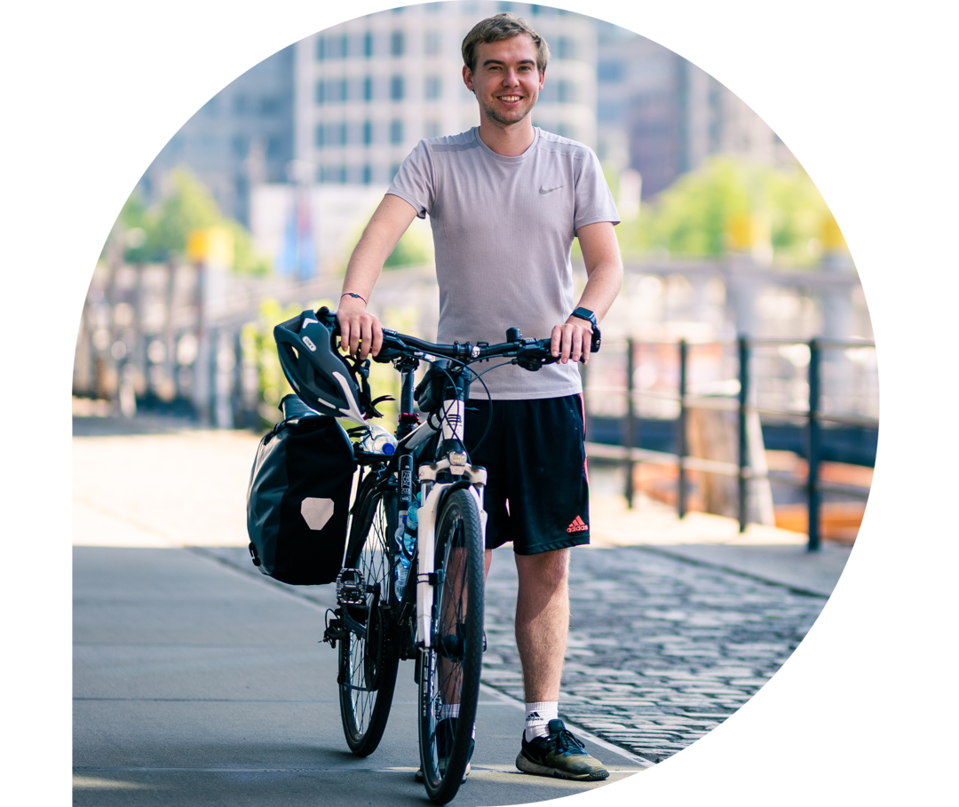 Phil Oliver Ladehof trägt ein weißes Shirt und hält ein Fahrrad mit Packtaschen fest. 