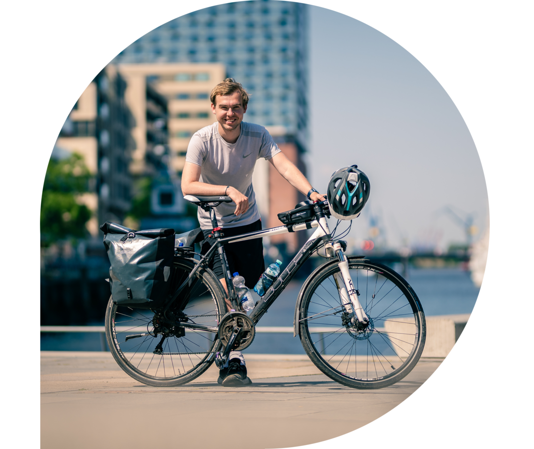 Phil Oliver steht mit seinem Fahrrad in der HafenCity in Hamburg, im Hintergrund die Elbphilharmonie. 