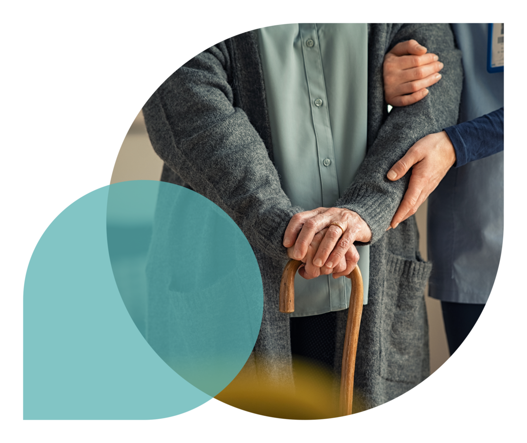 Zwei Personen, deren Gesichter nicht zu sehen sind, stehen nebeneinander. Die eine Person stützt die andere, die einen Gehstock in der Hand hält.