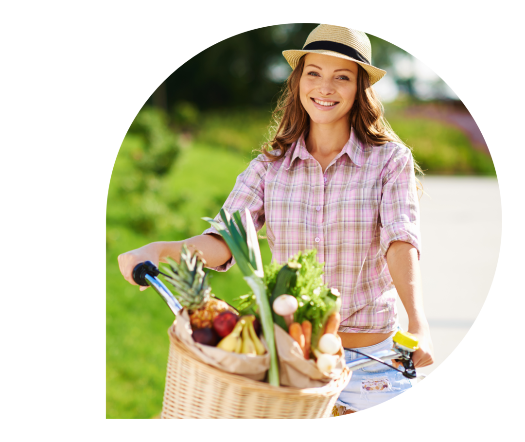 Eine Frau mit einem Fahrrad mit Obst und Gemüse im Fahrradkorb.