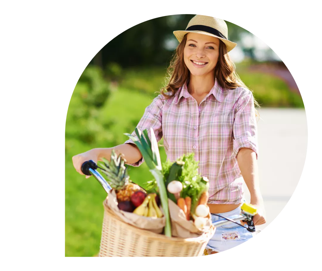Eine Frau mit einem Fahrrad mit Obst und Gemüse im Fahrradkorb.