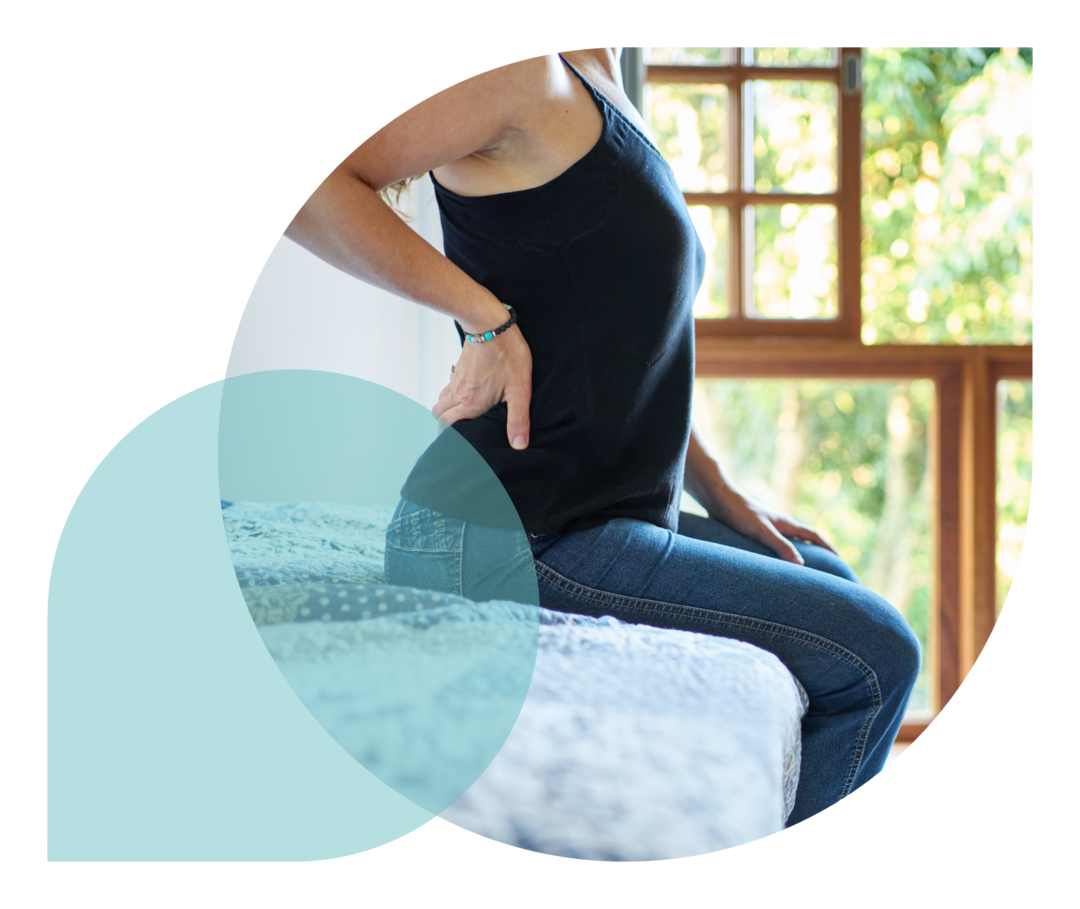 Eine Person sitzt auf einem Bett und hält sich den unteren Rücken.