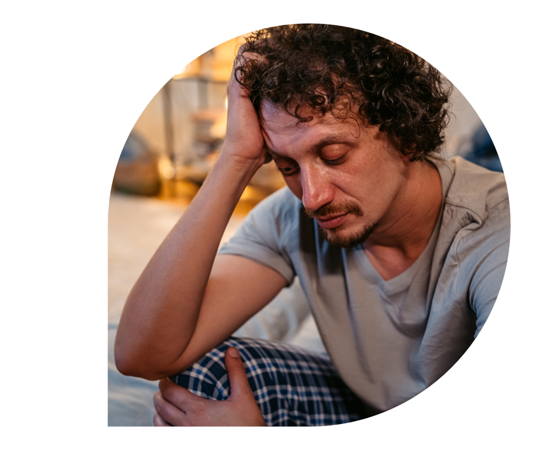 Ein Mann sitzt auf einem Bett und sieht müde aus.