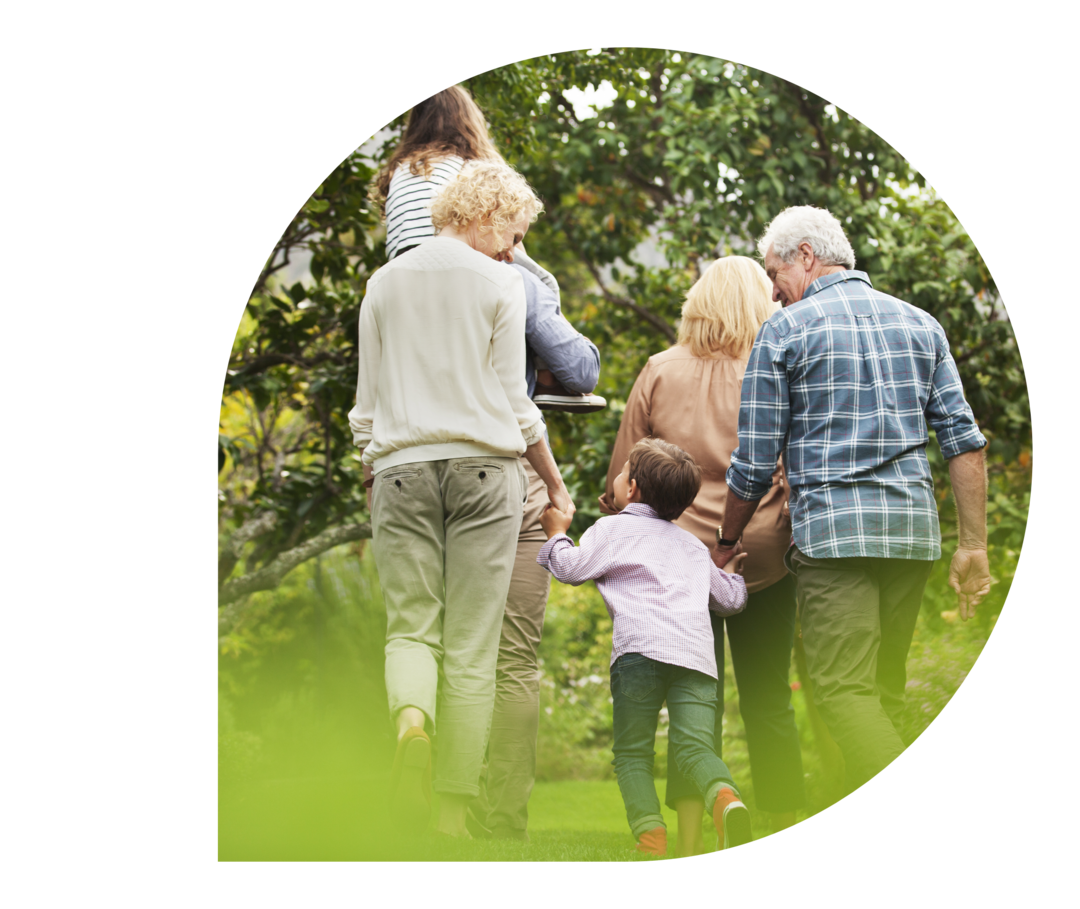Ratgeber Rheuma: Vererbung in der Familie Vor Bäumen und Büschen sind zwei Kinder und vier Erwachsene von hinten zu sehen. Zwei der Erwachse-nen halten die Hände eines der Kinder, das andere Kind sitzt auf den Schultern eines weiteren Erwachse-nen.