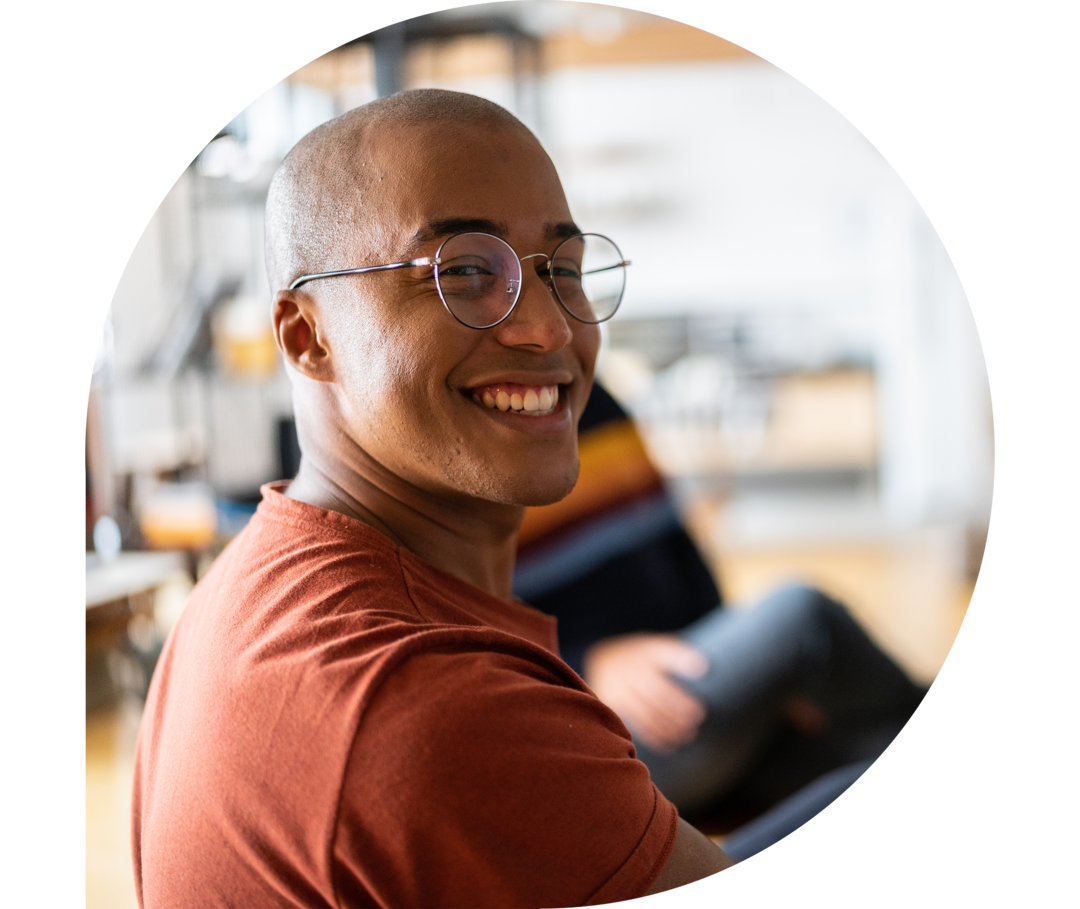 Ein junger Mann sitzt mit anderen Menschen in einem Kreis und lächelt in die Kamera.