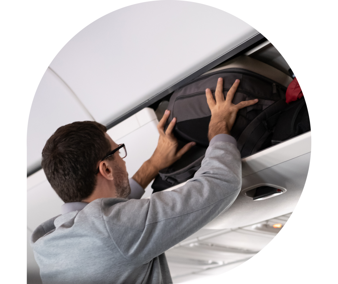 Ein Mann hebt seinen Koffer in das Gepäckfach eines Flugzeugs.