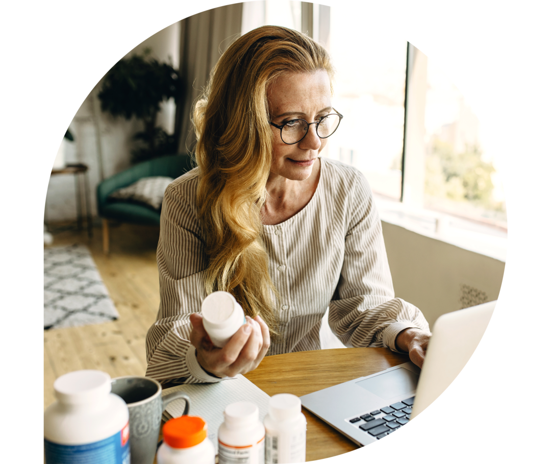 Eine Frau hält eine Medikamentendose in der Hand und schaut auf ein Notebook.