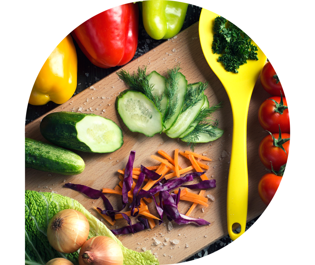 Unterschiedliche Gemüsesorten, eine Schneidebrett und ein gleber Löffel liegen auf einem Tisch.