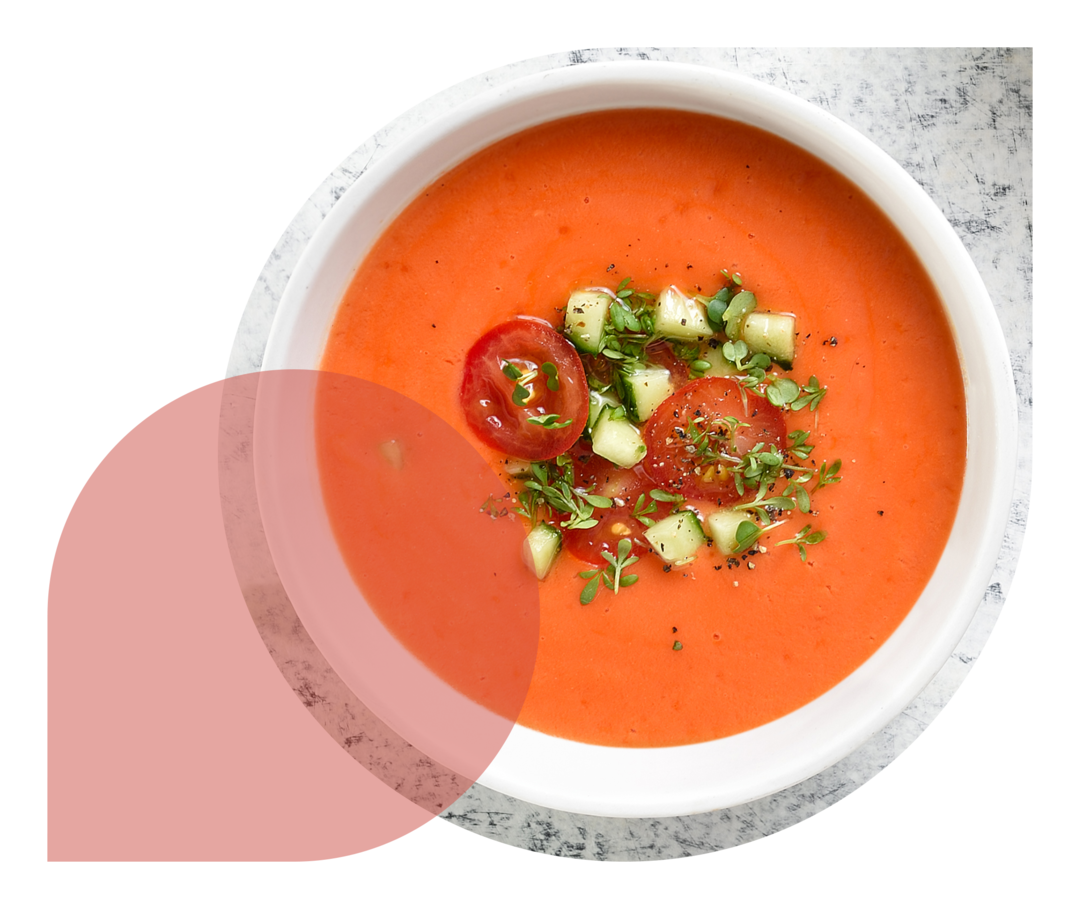 Auf einem hellen Tisch steht eine Schale mit rötlicher Suppe und Gemüseeinlage.