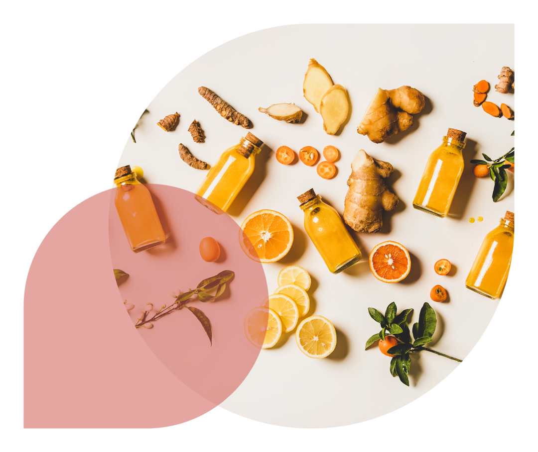 Rezepte für Rheumatiker*innen: Ingwer-Kurkuma-Shots Auf einem hellen Untergrund liegen ganze und aufgeschnittene Orangen, Ingwerknollen sowie Flaschen mit orangefarbener Flüssigkeit.