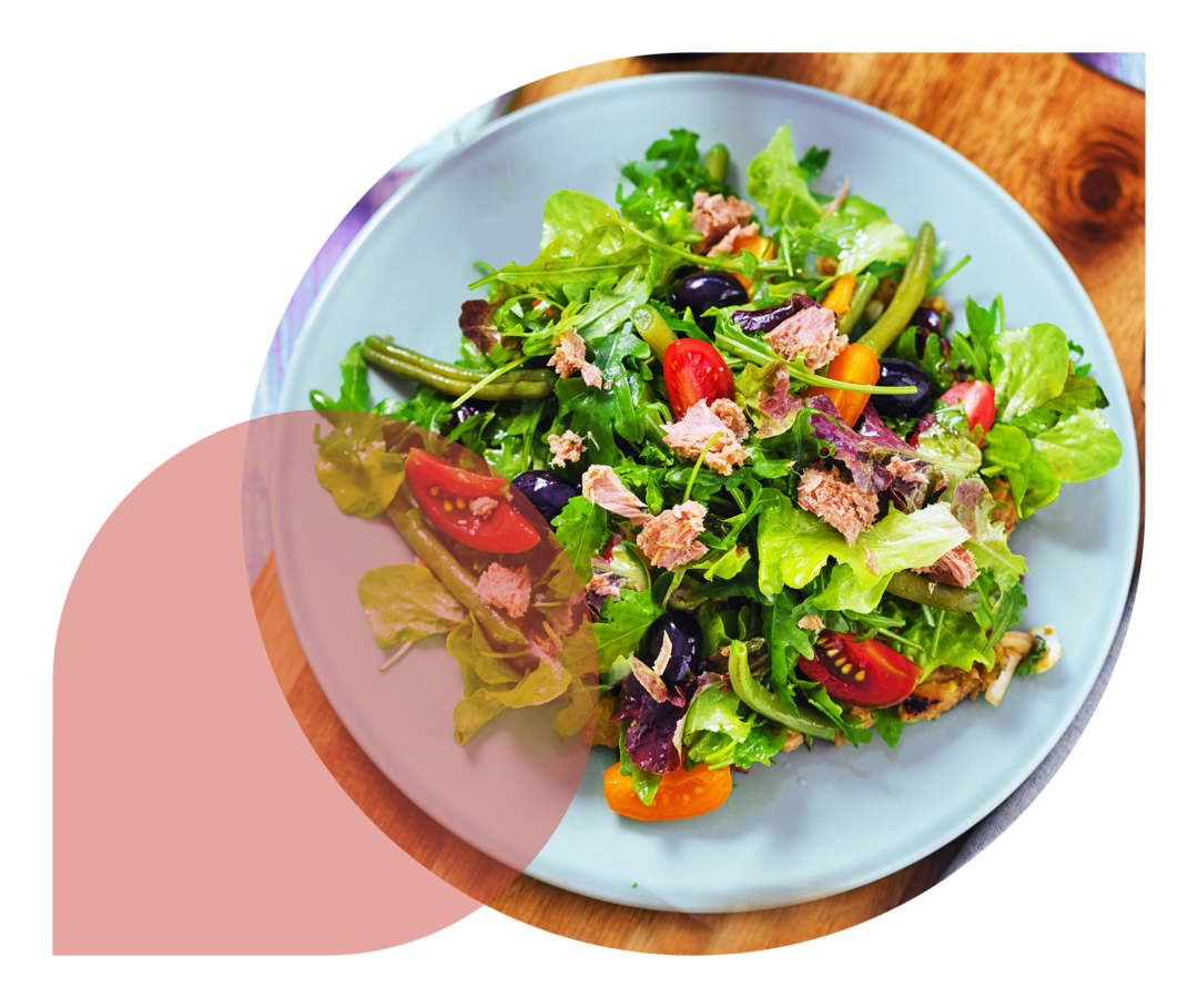 Auf einem Holzbrett steht ein weißer Teller mit einem gemischten Salat. Daneben liegt eine Gabel.