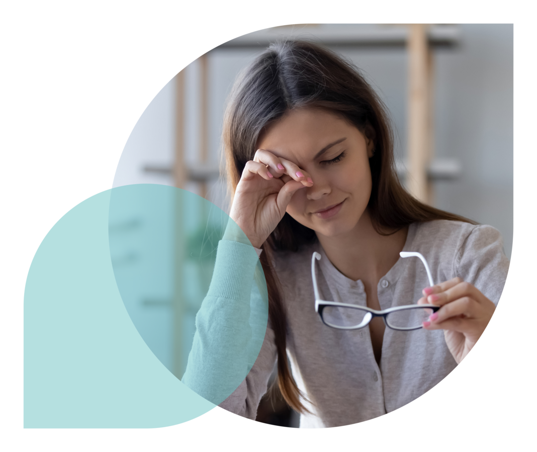 Eine Frau sitzt an einem Tisch, hat ihre Brille abgenommen und reibt sich ihr rechtes Auge.