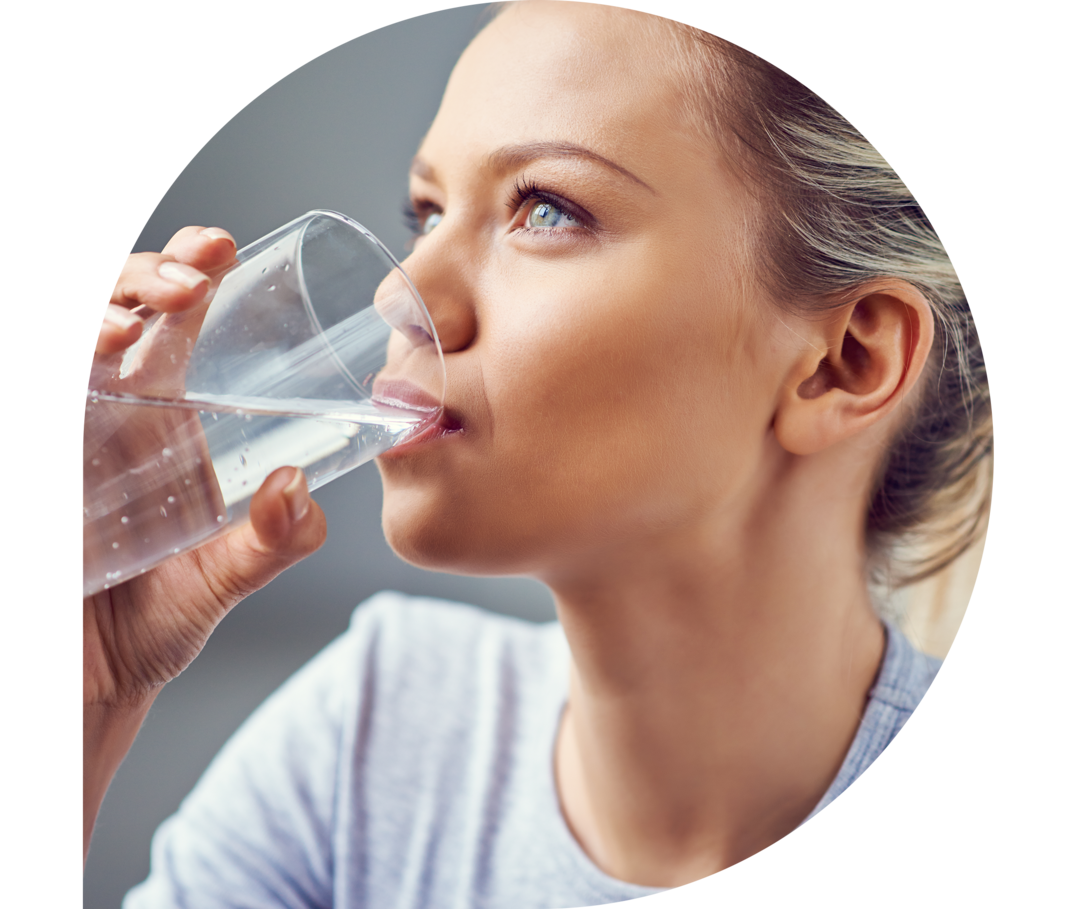 Eine junge Frau mit blonden Haaren trinkt Wasser aus einem Glas. 